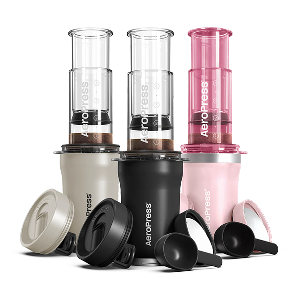 Aeropress coffee makers in beige, black, and pink on a white background