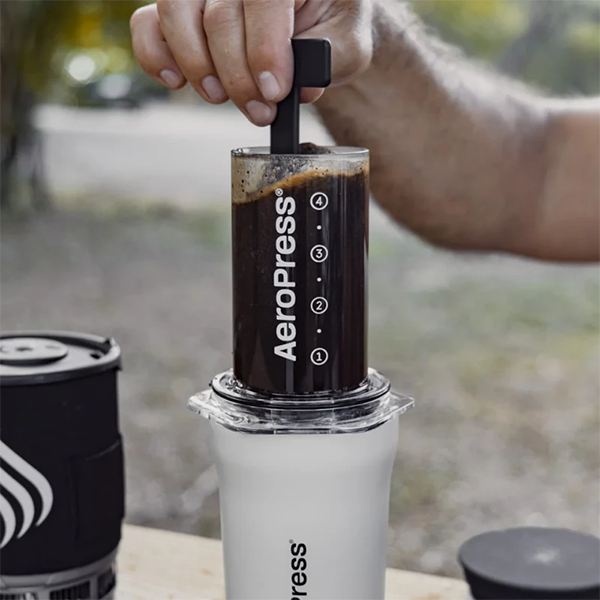 Person using an Aeropress outdoor with a blurred natural background