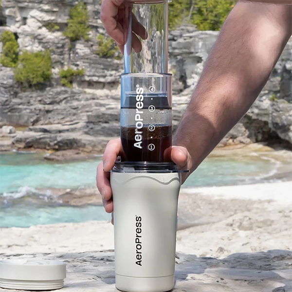 Person holding an Aeropress coffee maker with a scenic background
