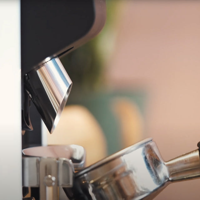 Close-up of a coffee machine dispensing coffee into a glass container.
