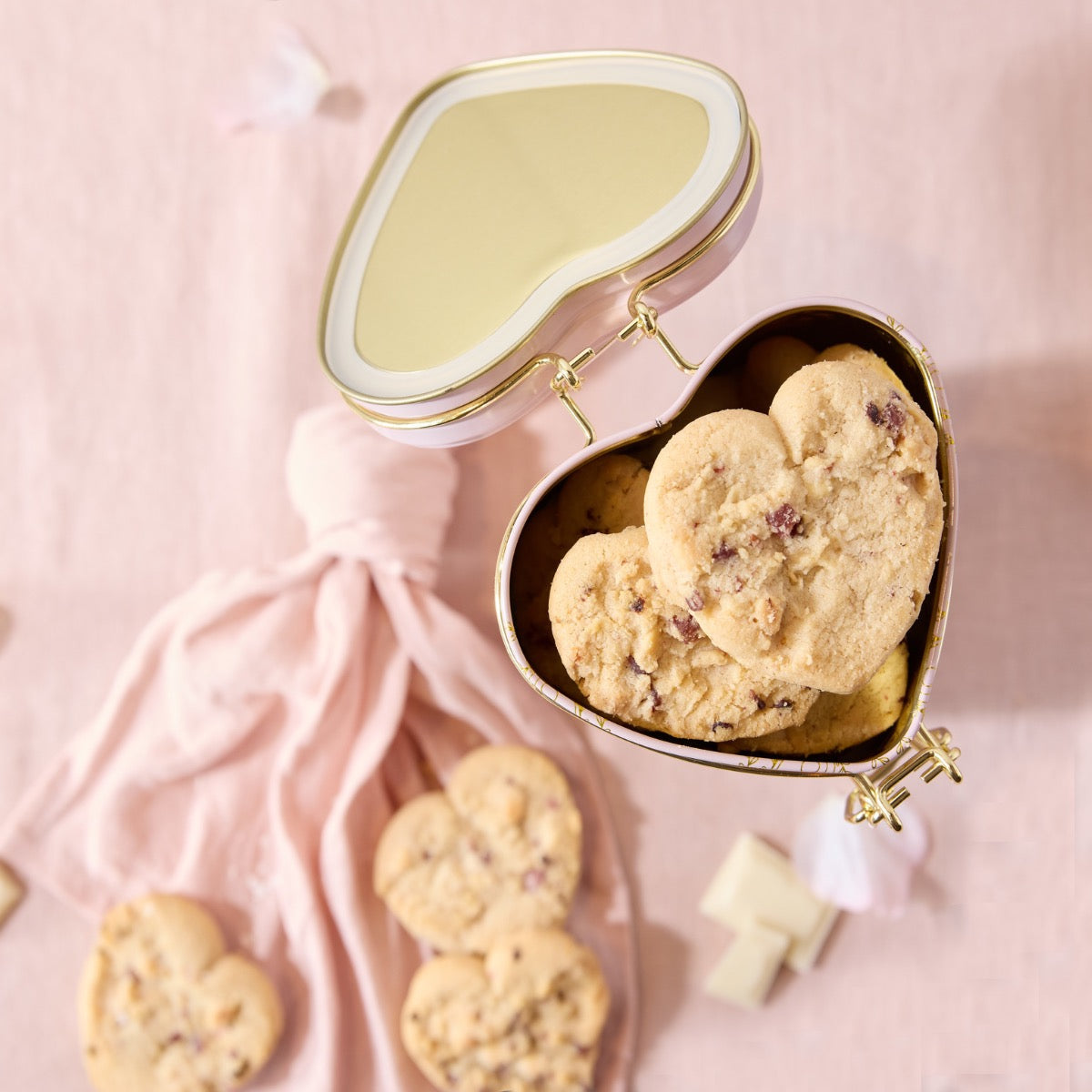 Heart-shaped cookie tin with cookies on a pink background