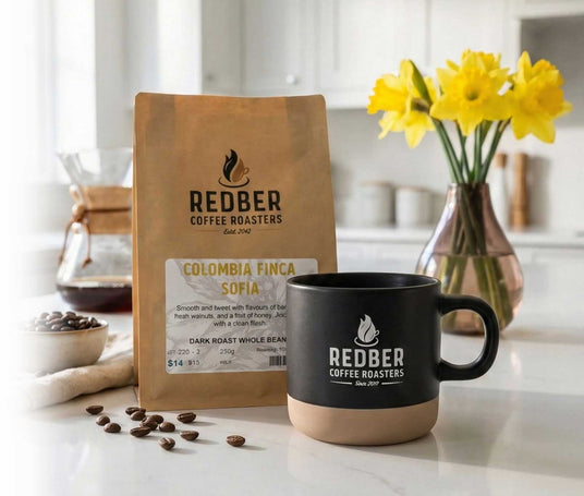 Redber Coffee Roasters package and mug on a kitchen counter with coffee beans and flowers.