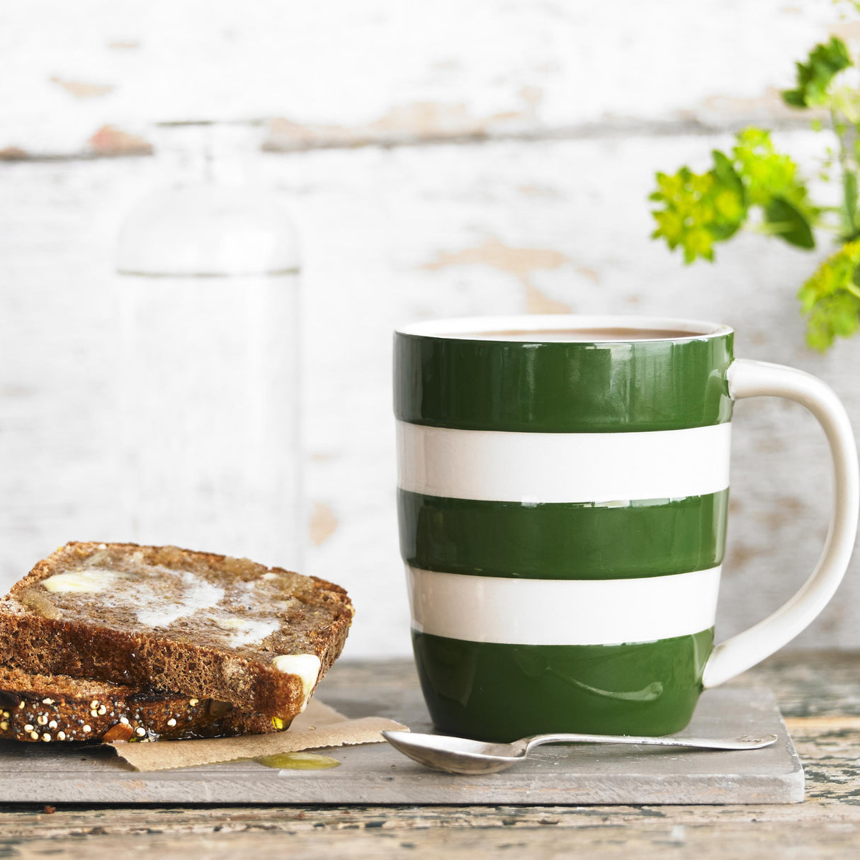 Green and white striped mug with toast and a spoon on a wooden surface