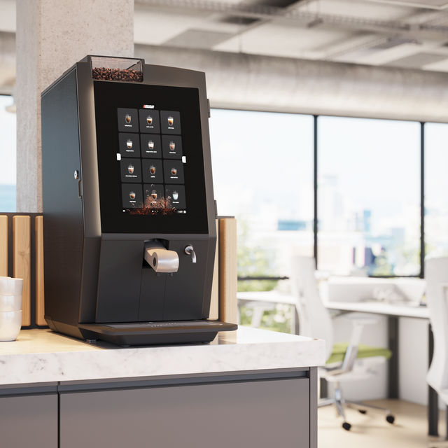 Coffee machine on a counter in an office setting with large windows.