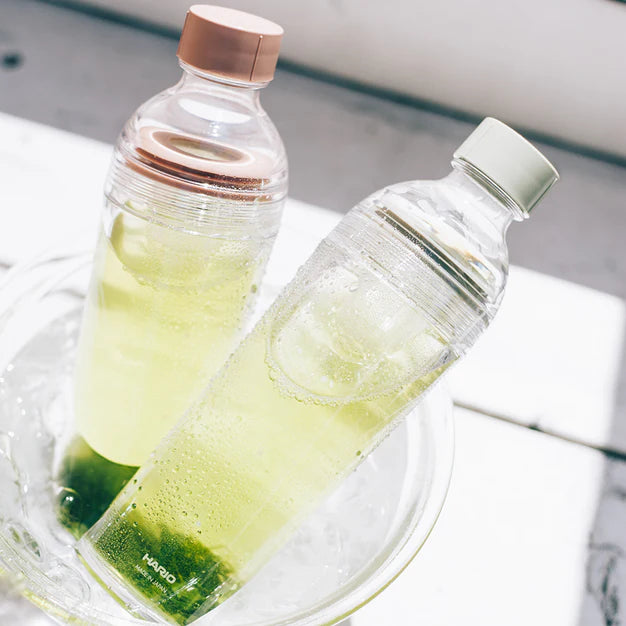 Two clear bottles with green liquid on a white surface