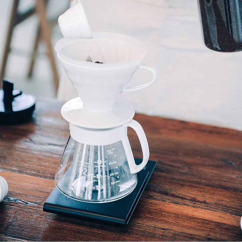 Person making coffee using a pour-over coffee maker on a wooden table.