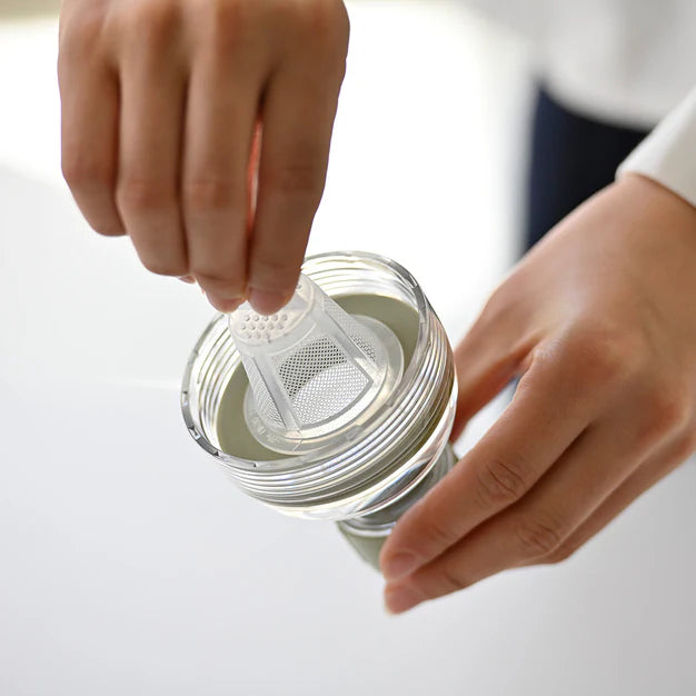 Person placing a white tea infuser into a glass of green tea.