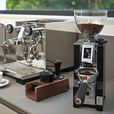 Coffee grinder with coffee beans on a countertop next to an espresso machine.