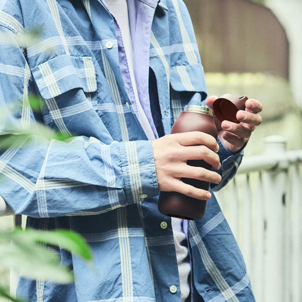 Person holding a brown bottle outdoors with blurred background