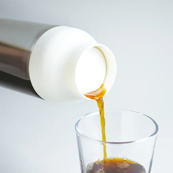 White container pouring coffee into a clear glass on a light gray background
