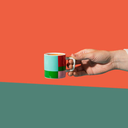 Hand holding a colorful mug against a split background of orange and green.