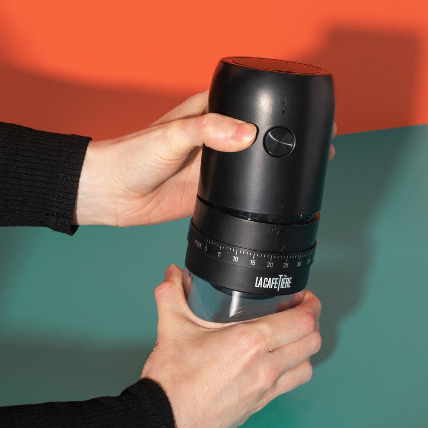 Person holding a black coffee grinder against a colorful background