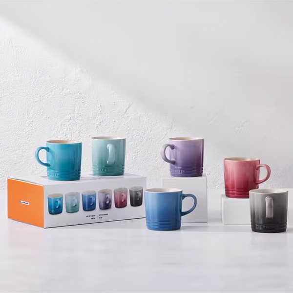 Set of colorful mugs with a packaging box on a light textured background
