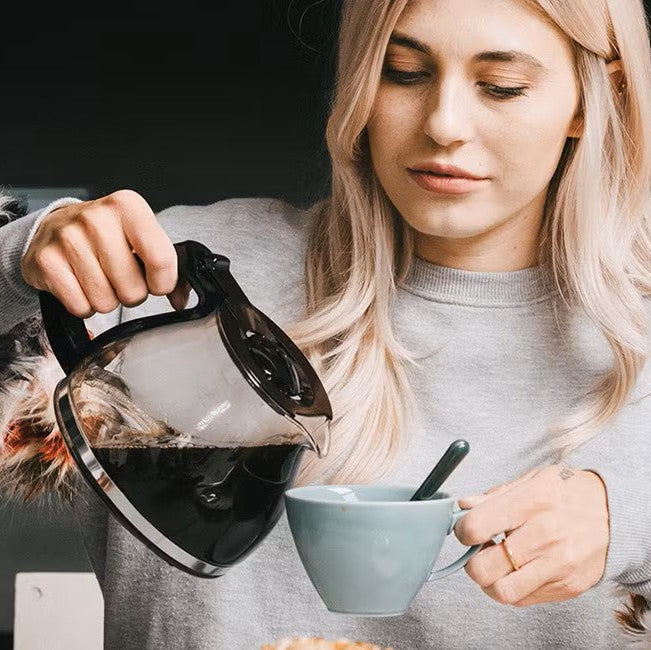 Woman pouring coffee from a kettle into a bowl with a spoon.