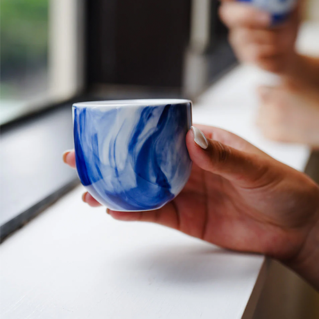 Hand holding a blue and white marbled ceramic cup with a blurred background