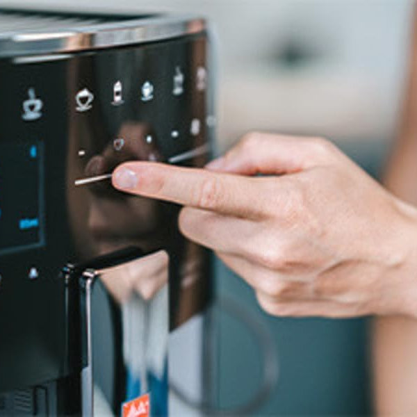 Hand pressing a button on a coffee machine with a blurred background