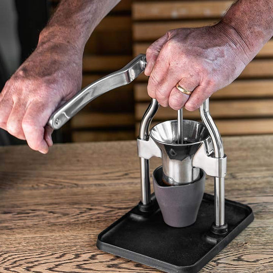 Person using a manual coffee press on a wooden surface