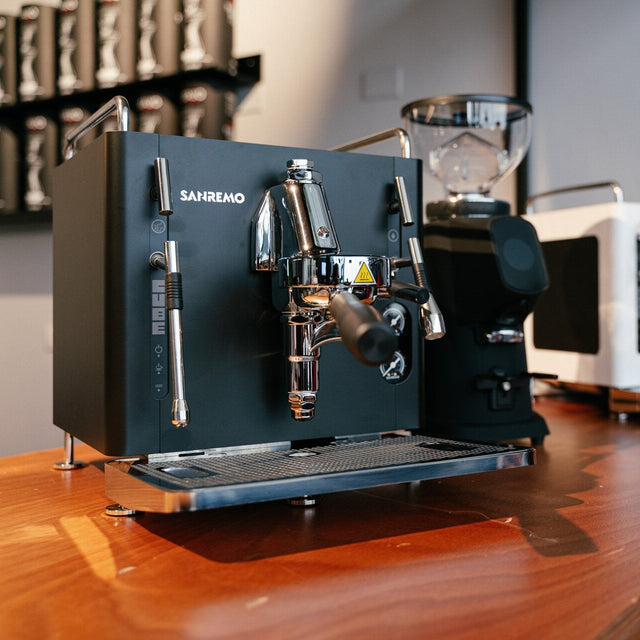 Black espresso machine on a wooden counter with a blurred kitchen background