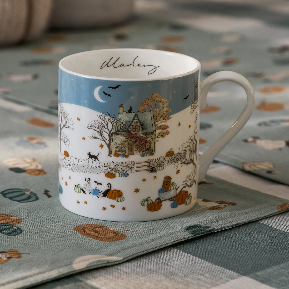 Decorative mug with autumn-themed design on a matching tablecloth.