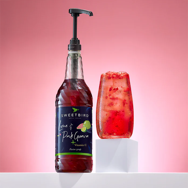 Bottle of Sweetbird syrup with a pump and a glass of red drink on a pink background