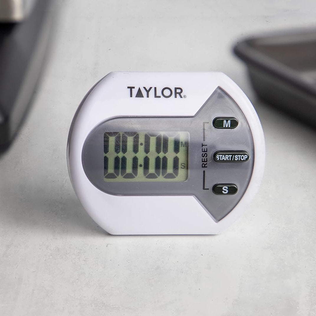 Taylor digital timer on a light gray surface with kitchen items in the background