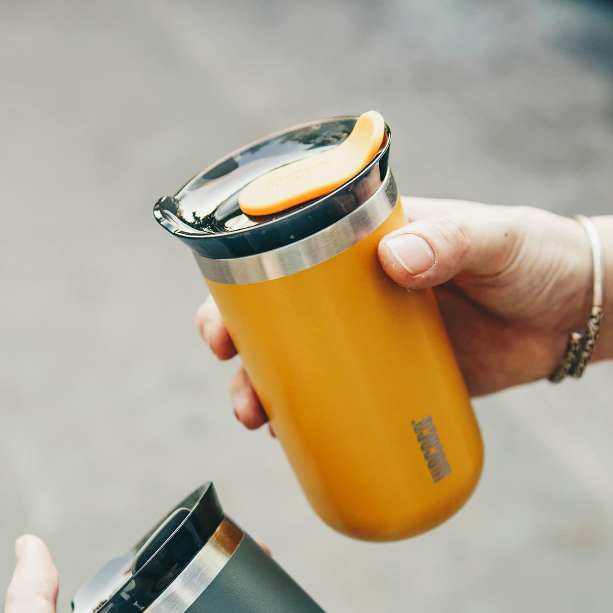 Person holding a mustard yellow insulated tumbler with a lid and apple slice.