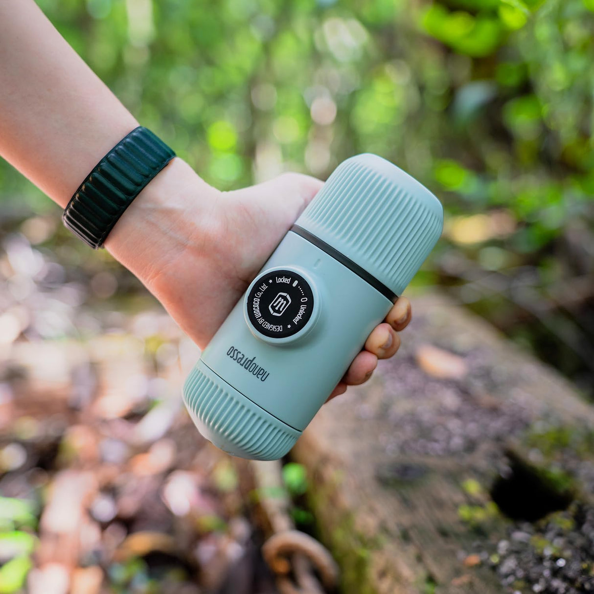 Hand holding a light blue travel mug with a blurred natural background