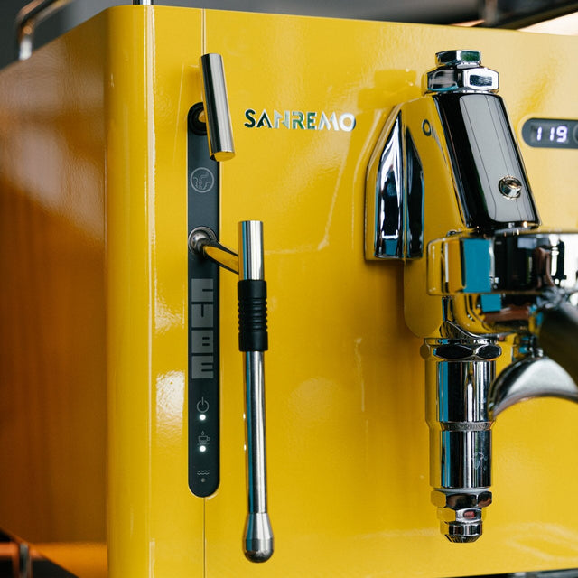 Yellow espresso machine with 'Sanremo' branding on a wooden surface.