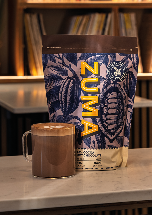 Zuma hot chocolate bag with a mug of hot chocolate on a surface.