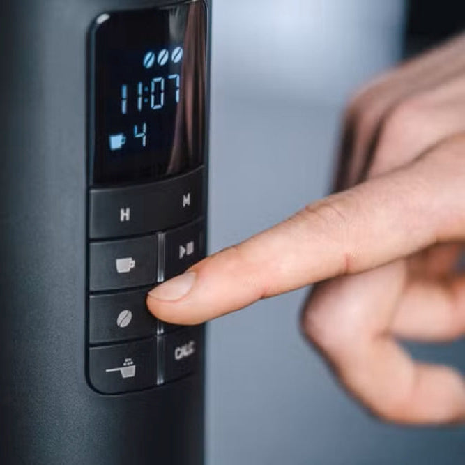 Person pressing a button on a coffee machine control panel