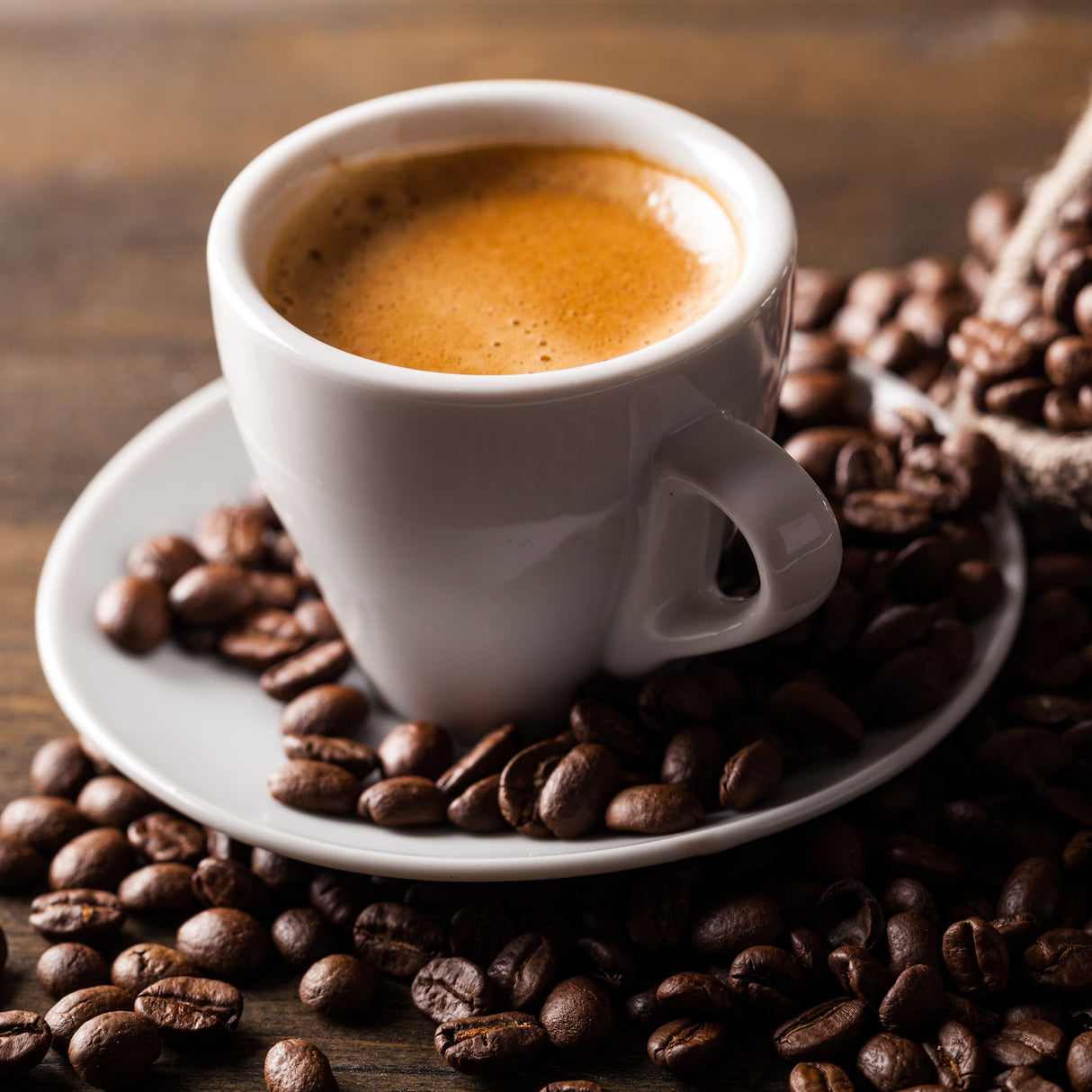White cup of espresso surrounded by coffee beans on a wooden surface