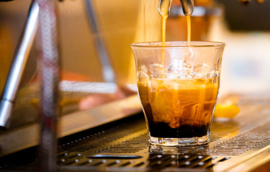 Espresso being poured into a glass on a bar.