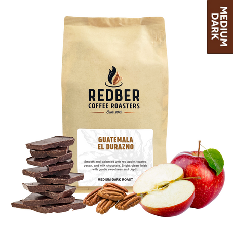 A bag of Guatemala El Durazno medium-dark roast coffee from Redber Coffee Roasters, accompanied by chocolate pieces, apples, and pecans, indicating the flavor profile of the coffee.