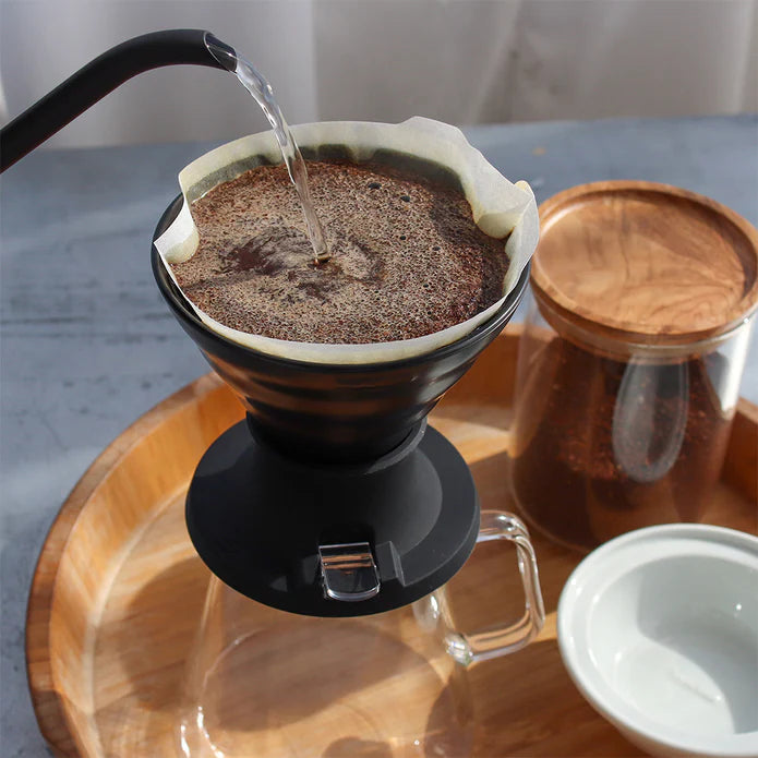 Coffee being poured into a filter on a wooden tray with a glass container in the background.