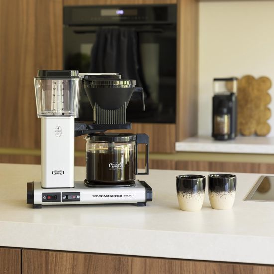 Coffee maker on a kitchen counter with two cups nearby