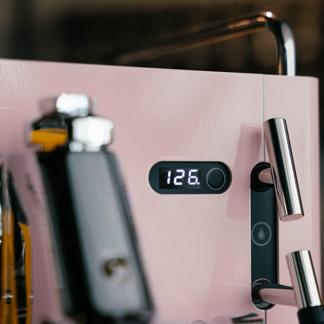 Close-up of a pink coffee machine with a digital display showing '126.' on a blurred background.