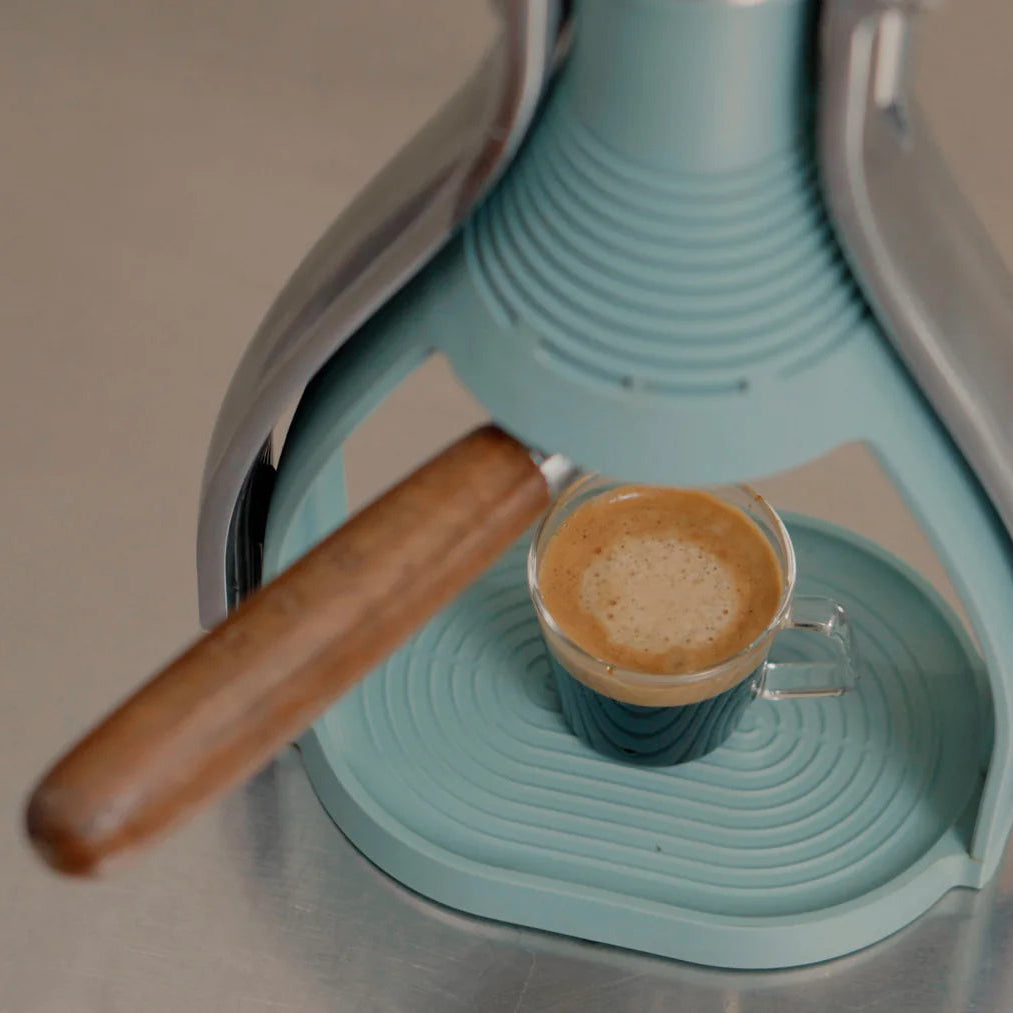 Espresso cup with a wooden handle on a turquoise and gray coffee machine.