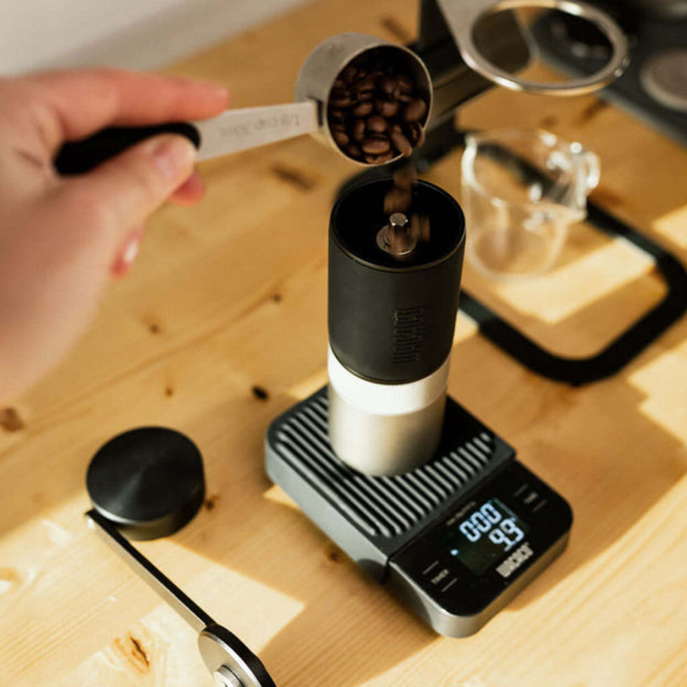 Adding coffee beans to a Wacaco Exagrind grinder at a coffee preparation station