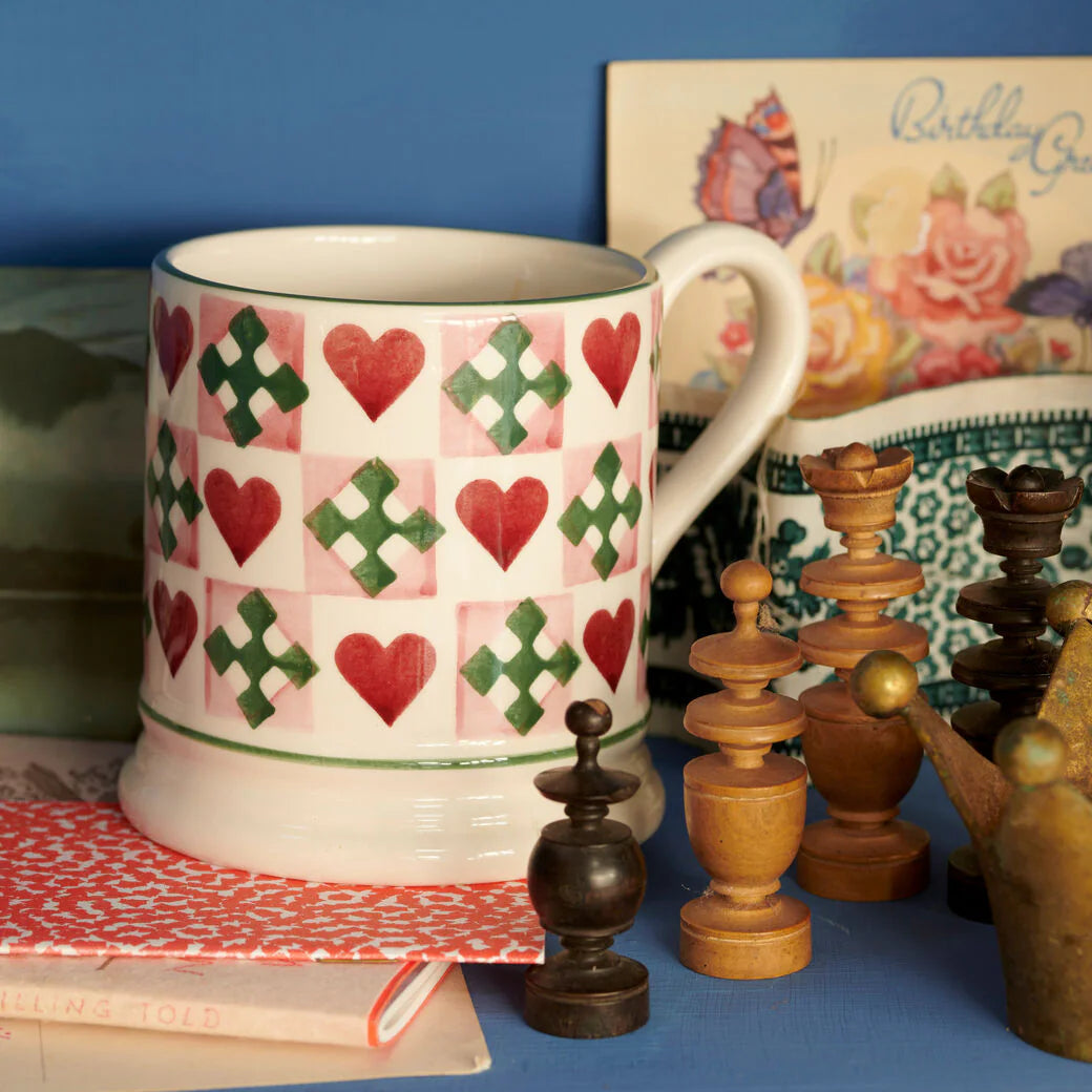 Emma Bridewater Mug with heart and cross pattern on a blue surface with decorative items.