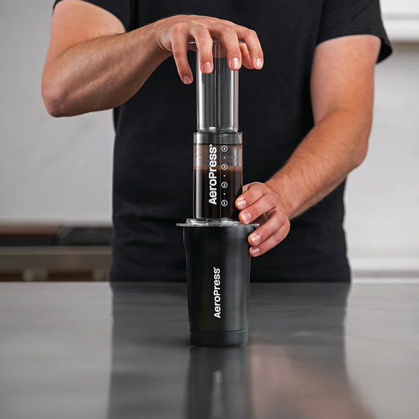 Person holding an AeroPress coffee maker on a countertop
