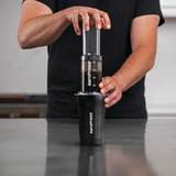Person holding an AeroPress coffee maker on a countertop