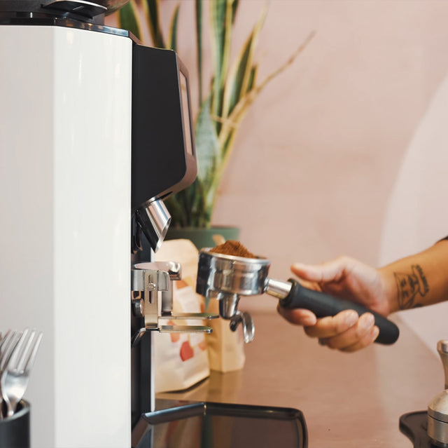 Person using a coffee machine with a focus on the hand and coffee grinder.