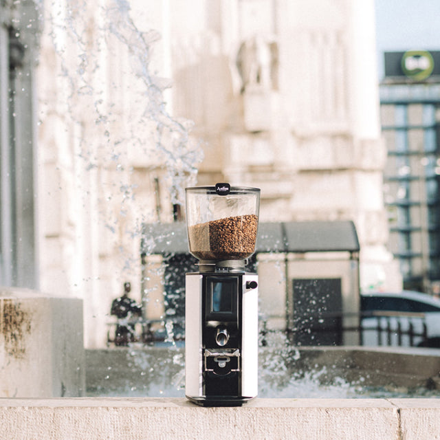 Coffee grinder with coffee beans on a ledge with a cityscape background