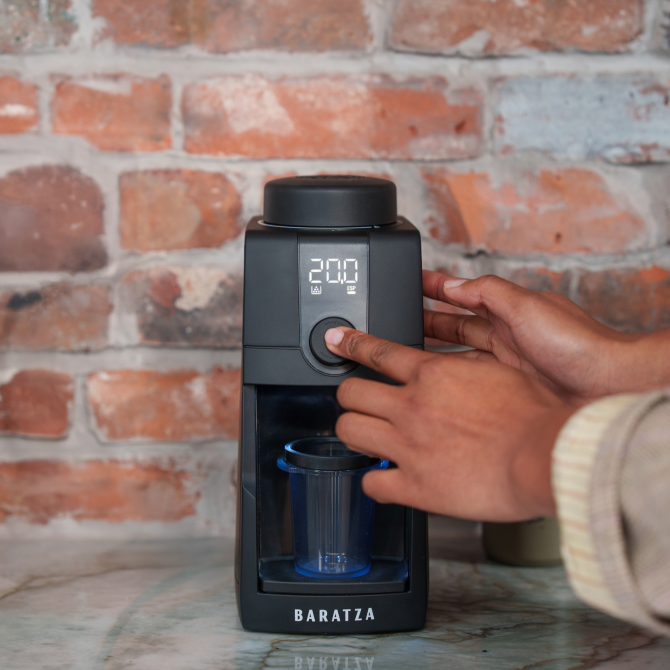Person using a Baratza coffee grinder against a brick wall.