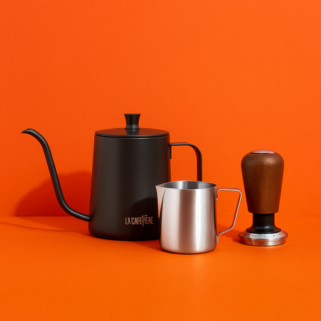 Black gooseneck kettle, silver milk pitcher, and brown coffee grinder on an orange background