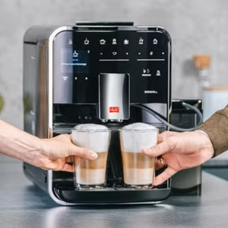 Espresso machine dispensing coffee into two glasses held by a person.