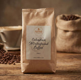 Brown paper bag of Redber Colombian Microground Coffee on a wooden surface with coffee beans and a cup in the background.