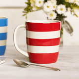 Red and white striped mug on a table with a spoon and blurred flowers in the background