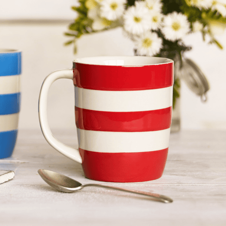 Red and white striped mug on a table with a spoon and blurred flowers in the background