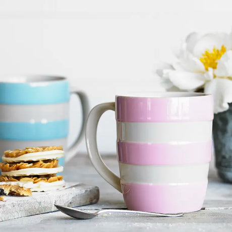 Colorful striped mugs on a table with a spoon and cookies.